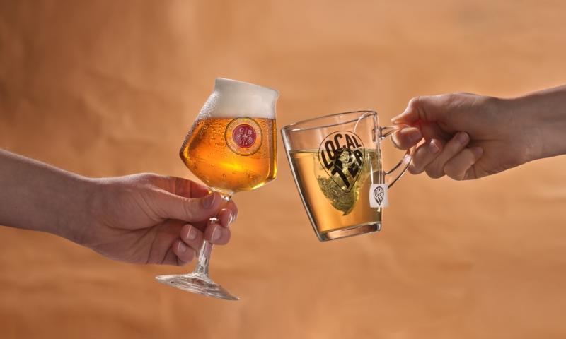 Handen met glazen Grolsch Blont en thee proosten